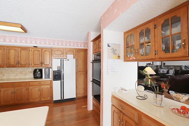 kitchen with white refrigerator with ice dispenser, dark wood-style flooring, light countertops, brown cabinets, and glass insert cabinets