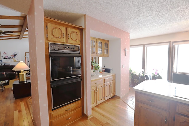 kitchen featuring light wood-type flooring, light countertops, a textured ceiling, and dobule oven black