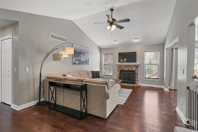 living room with dark hardwood / wood-style flooring, a stone fireplace, vaulted ceiling, and ceiling fan