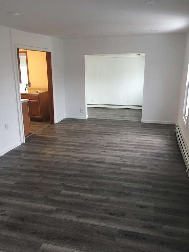 empty room with dark wood-type flooring, sink, and a baseboard heating unit