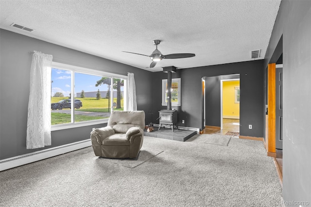 1408 Stephens Ave, Flint, MI 48507 - living area featuring a wood stove, a textured ceiling, a ceiling fan, a baseboard radiator, and carpet floors