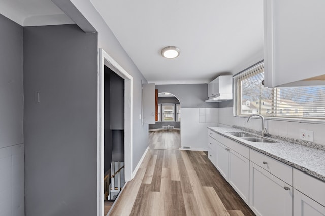 kitchen with sink, light stone counters, white cabinets, and light hardwood / wood-style floors