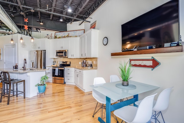 dining space featuring a high ceiling, sink, track lighting, and light wood-type flooring