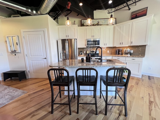 kitchen with a breakfast bar, white cabinetry, a kitchen island with sink, stainless steel appliances, and light stone countertops