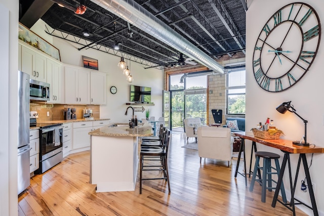 kitchen featuring sink, appliances with stainless steel finishes, white cabinetry, light stone countertops, and a center island with sink