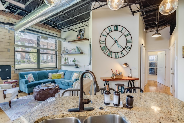 kitchen with sink, a towering ceiling, light hardwood / wood-style flooring, and light stone countertops