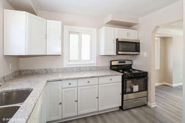 kitchen featuring sink, appliances with stainless steel finishes, light stone countertops, light hardwood / wood-style floors, and white cabinets