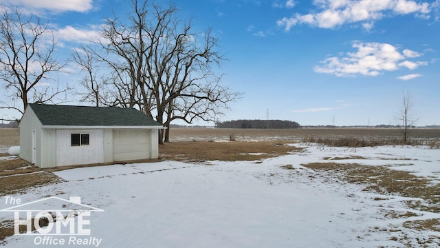 yard covered in snow with a rural view, a garage, and an outdoor structure