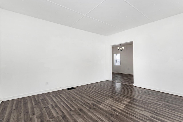 empty room with dark hardwood / wood-style floors and a notable chandelier
