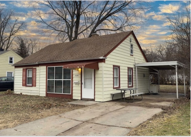 view of front of house featuring a shingled roof, an attached carport, and a chimney