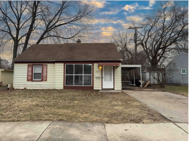 bungalow featuring a carport, driveway, a shingled roof, and a chimney