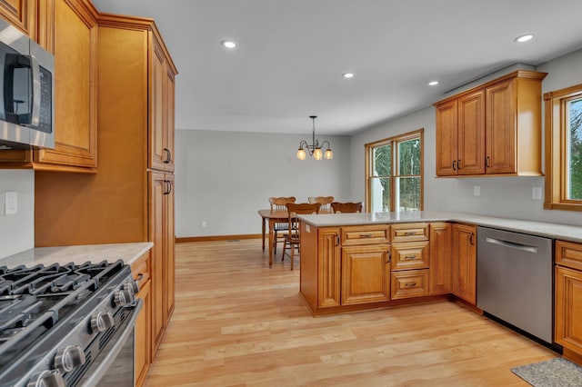 kitchen with appliances with stainless steel finishes, decorative light fixtures, light hardwood / wood-style floors, an inviting chandelier, and kitchen peninsula