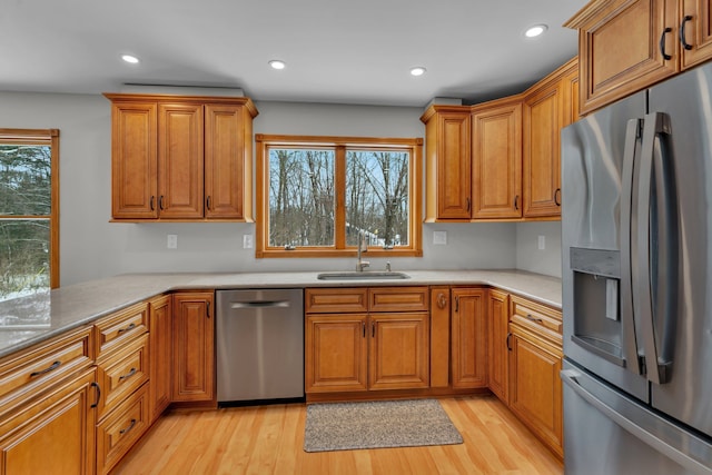 kitchen with appliances with stainless steel finishes, sink, kitchen peninsula, and light wood-type flooring