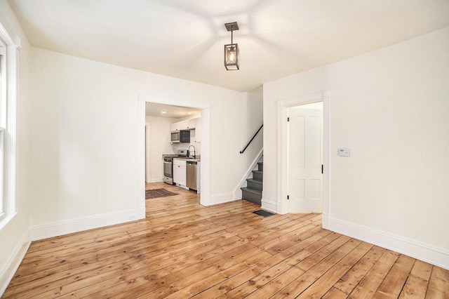 spare room featuring light wood-style floors, baseboards, and stairway