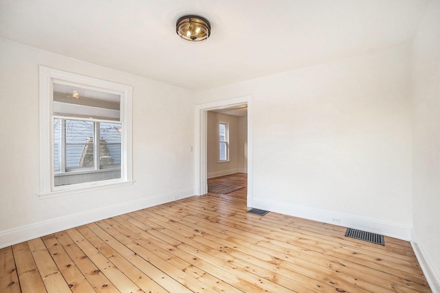 spare room featuring light wood-type flooring, plenty of natural light, and visible vents