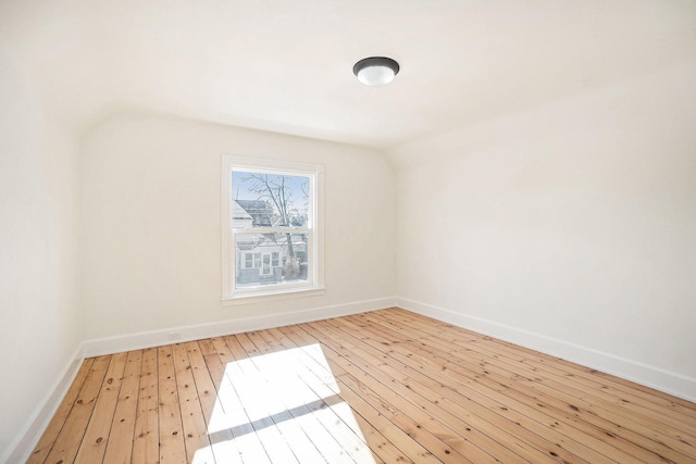 unfurnished room featuring light wood-style floors, baseboards, and vaulted ceiling