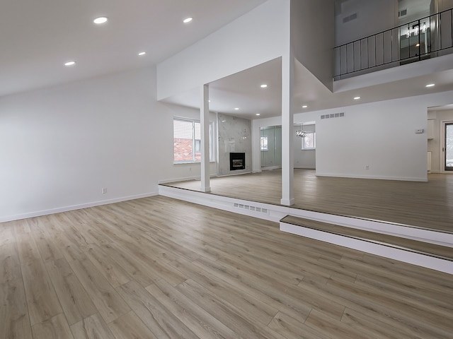 unfurnished living room with high vaulted ceiling, recessed lighting, light wood-style floors, a fireplace, and baseboards