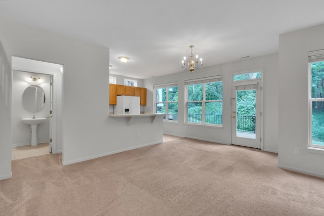 unfurnished living room with a chandelier, sink, and light carpet