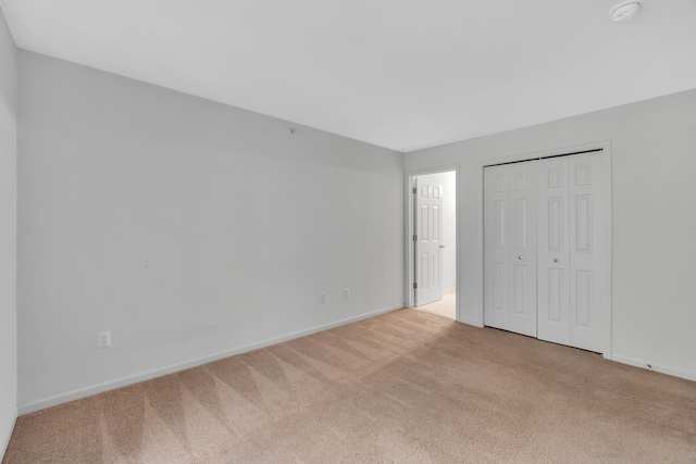 unfurnished bedroom with light colored carpet and a closet