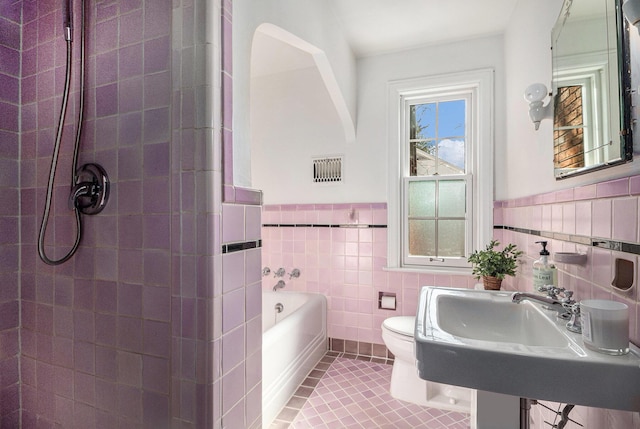 bathroom featuring tile walls, tile patterned floors, a tub, and toilet