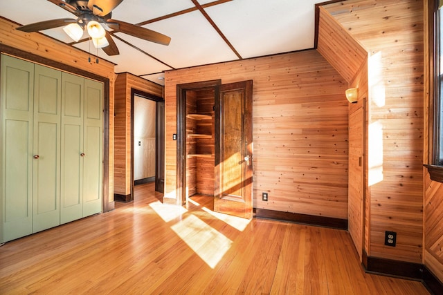 unfurnished bedroom with ceiling fan, light wood-type flooring, and wooden walls