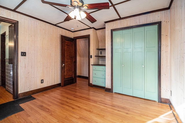 unfurnished bedroom featuring crown molding, wood walls, a closet, and light wood-type flooring