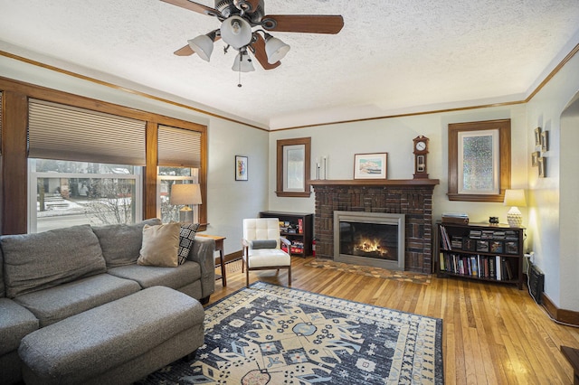 living room featuring crown molding, a textured ceiling, ceiling fan, a fireplace, and light hardwood / wood-style floors