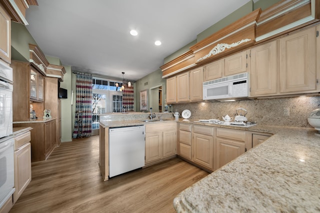 kitchen with white appliances, light wood finished floors, a peninsula, a sink, and backsplash