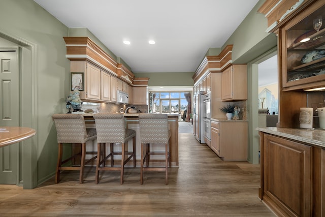 kitchen with decorative backsplash, white microwave, light wood-style flooring, a peninsula, and a kitchen bar