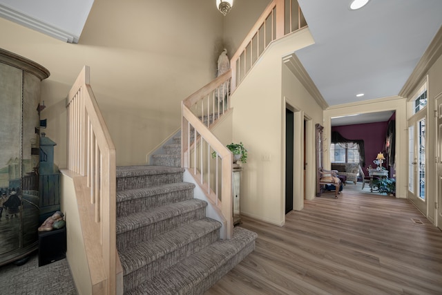 staircase with recessed lighting, a high ceiling, ornamental molding, wood finished floors, and baseboards