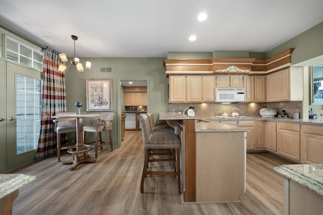 kitchen with visible vents, backsplash, white microwave, light wood-style floors, and light brown cabinets