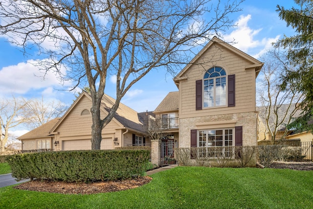 traditional-style house with an attached garage, a balcony, brick siding, fence, and a front lawn