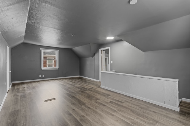 bonus room featuring lofted ceiling, hardwood / wood-style flooring, and a textured ceiling