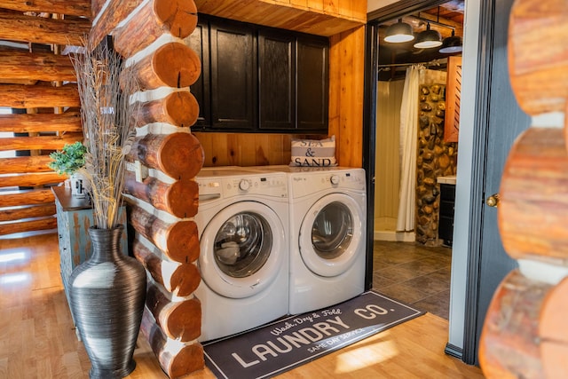 laundry room with cabinets, rustic walls, washing machine and dryer, and light hardwood / wood-style flooring