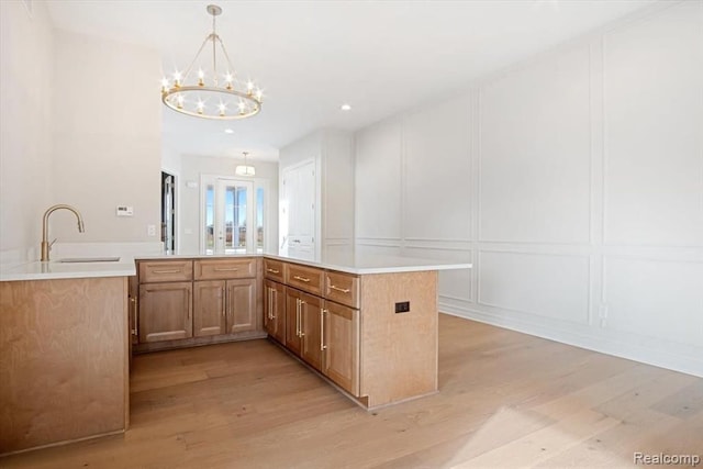 kitchen featuring decorative light fixtures, sink, a chandelier, kitchen peninsula, and light wood-type flooring