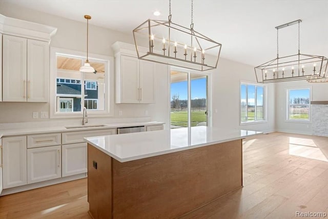 kitchen with sink, hanging light fixtures, light hardwood / wood-style floors, white cabinets, and a kitchen island