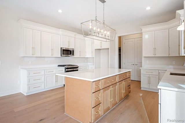 kitchen with decorative light fixtures, a center island, light wood-type flooring, appliances with stainless steel finishes, and white cabinets