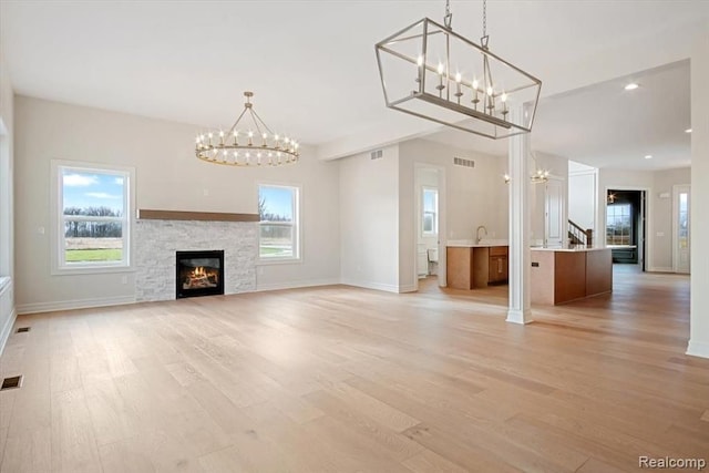 unfurnished living room with sink, light wood-type flooring, a chandelier, and a fireplace