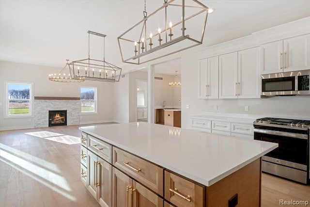 kitchen featuring white cabinetry, a center island, hanging light fixtures, light wood-type flooring, and stainless steel appliances