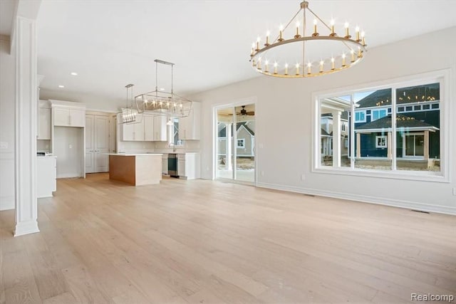 unfurnished living room featuring a wealth of natural light, sink, ceiling fan with notable chandelier, and light hardwood / wood-style flooring