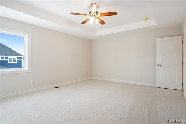 empty room with a raised ceiling, light carpet, and ceiling fan