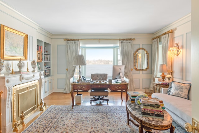 office with light hardwood / wood-style flooring, built in shelves, ornamental molding, and a fireplace