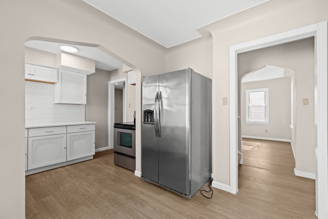 kitchen with backsplash, appliances with stainless steel finishes, light hardwood / wood-style flooring, and white cabinets