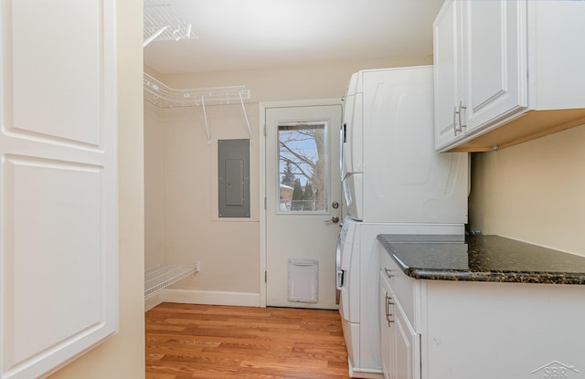 laundry area with stacked washer / dryer, electric panel, cabinets, and light hardwood / wood-style floors