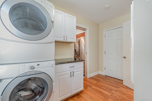 washroom featuring cabinets, stacked washer / drying machine, and light hardwood / wood-style flooring