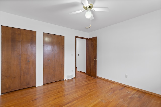 unfurnished bedroom featuring ceiling fan, two closets, and light wood-type flooring