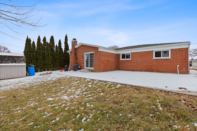 snow covered rear of property with a patio area and a shed