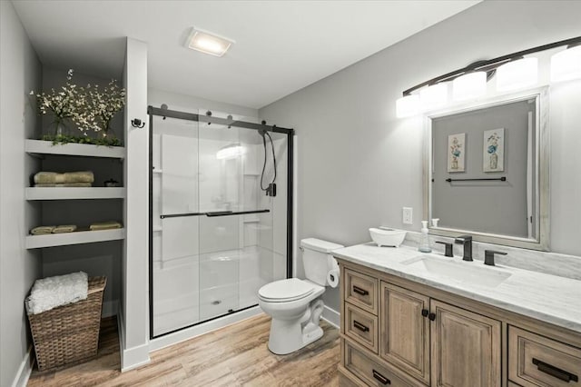 bathroom featuring toilet, a stall shower, vanity, wood finished floors, and baseboards