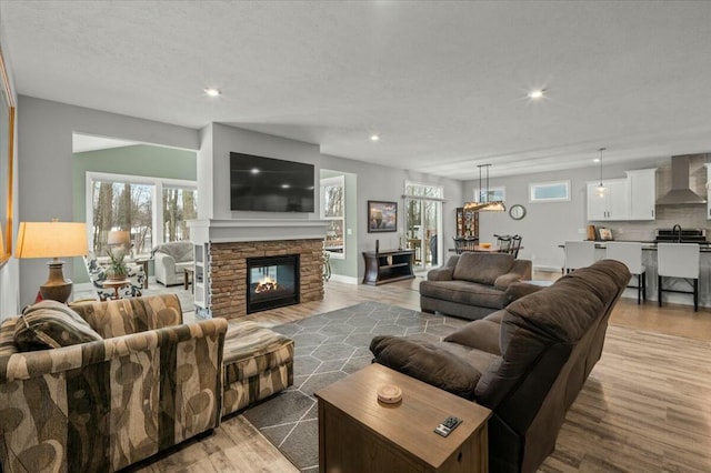 living area featuring a textured ceiling, a stone fireplace, light wood-style flooring, and recessed lighting