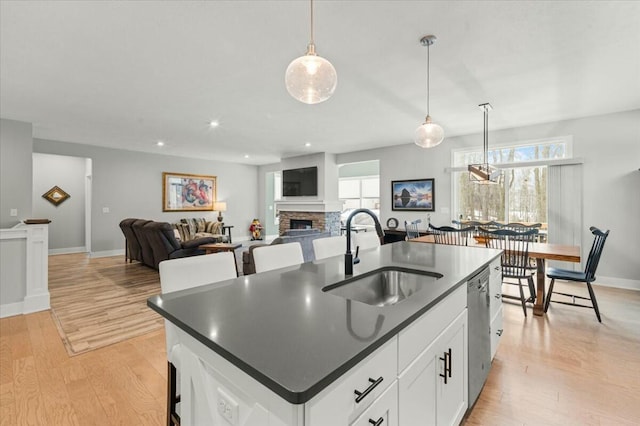 kitchen featuring a fireplace, a wealth of natural light, light wood-style flooring, a sink, and dishwasher